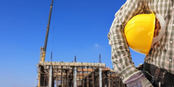 Worker standing with a hard hat under their arm in front of a construction site