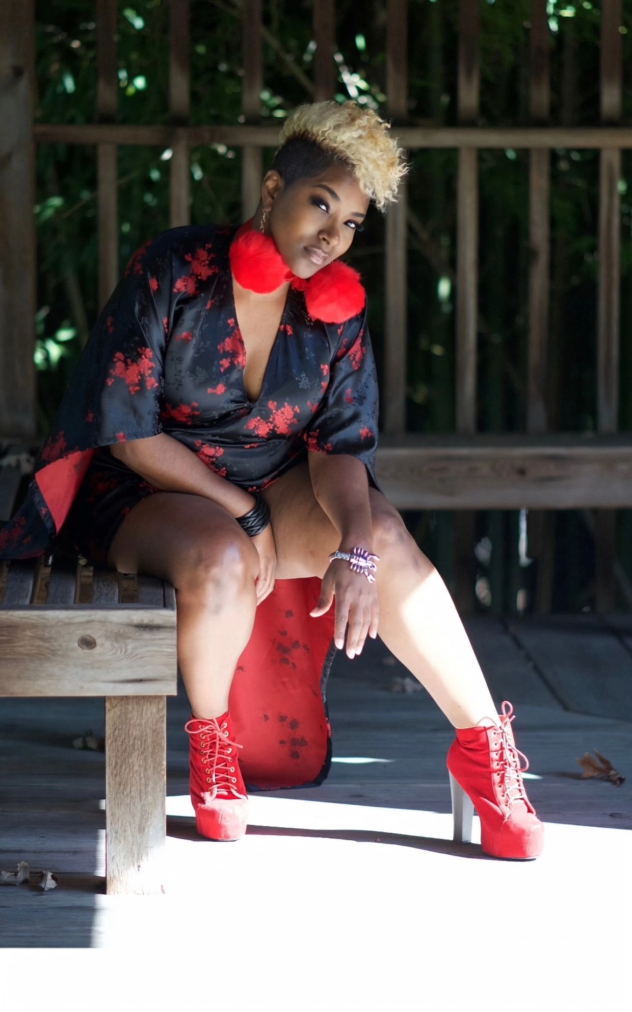 Woman in black and red outfit with red boots and fluffy earrings posing on a wooden bench.