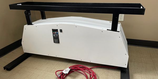 A white rectangular machine with a red coiled cable on the floor.