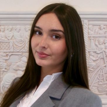 Young woman with long brown hair in grey blazer.