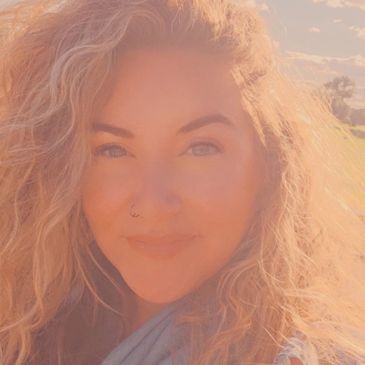 Smiling woman with curly hair in warm sunlight.