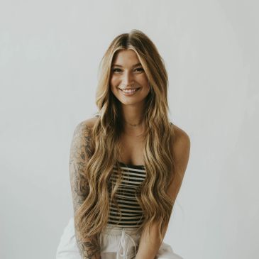 Smiling woman with long wavy hair and tattoo.