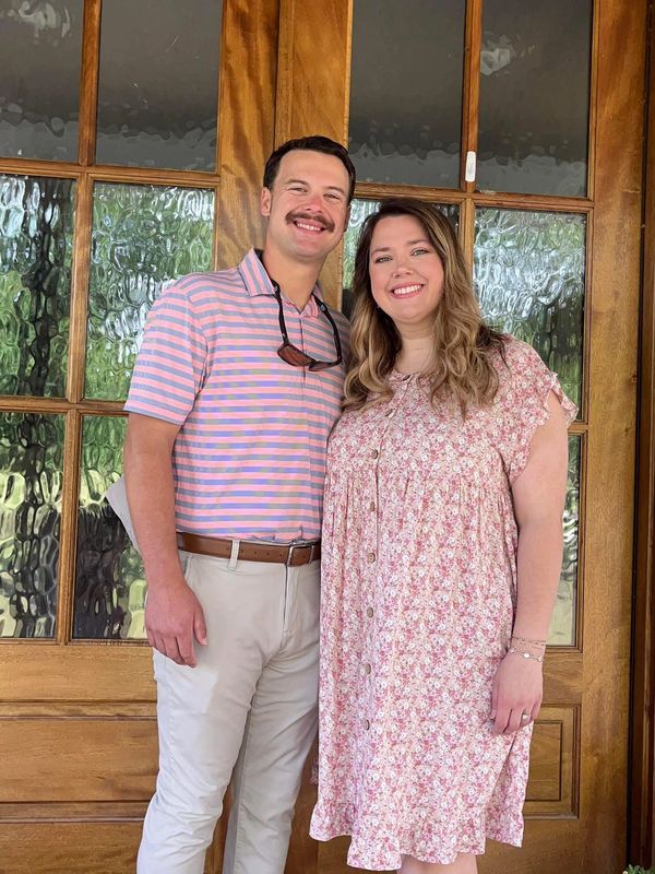 A smiling couple stands in front of a wooden door with glass panels.