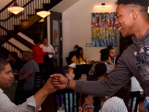 Two men fist bump in a lively restaurant.