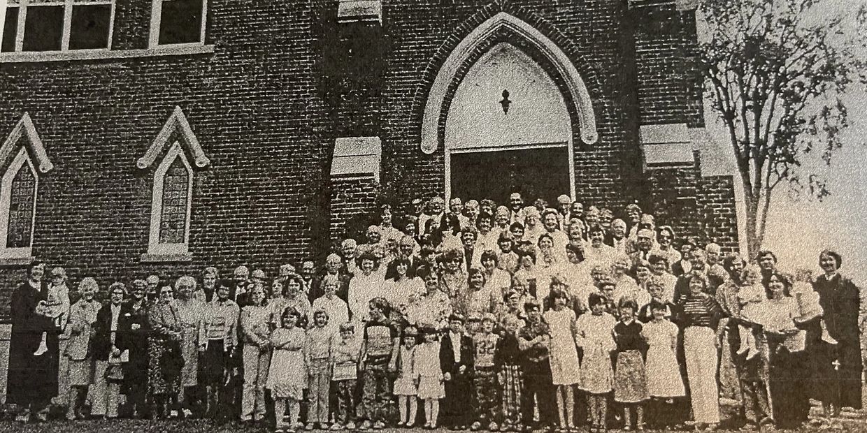 Black and white photo of congregation standing outside of church on front steps.