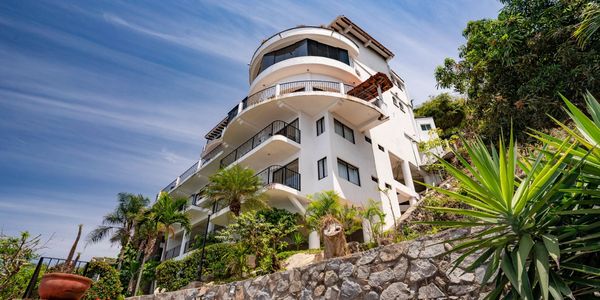 view of Puerto Vallarta rental house with balconies surrounded by tropical plants and a stone wall. vacation home in puerto vallarta mexico