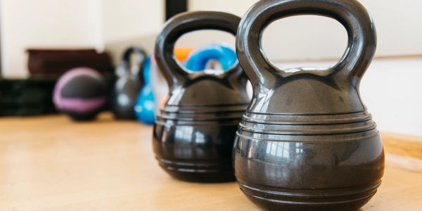 Two black kettlebells on a wooden floor in a gym setting.
