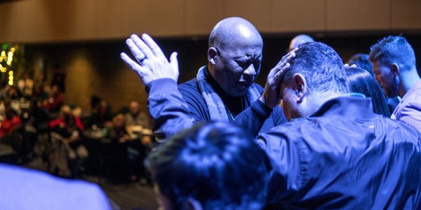 A man prays over another man in a gathering.