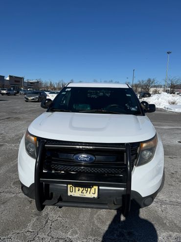 Front view of a white Ford vehicle with a push bumper in a parking lot on a clear day.