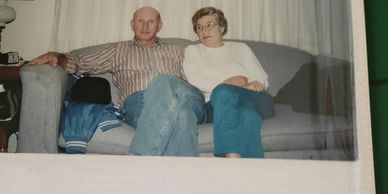 An elderly couple sitting closely on a sofa in a cozy room.