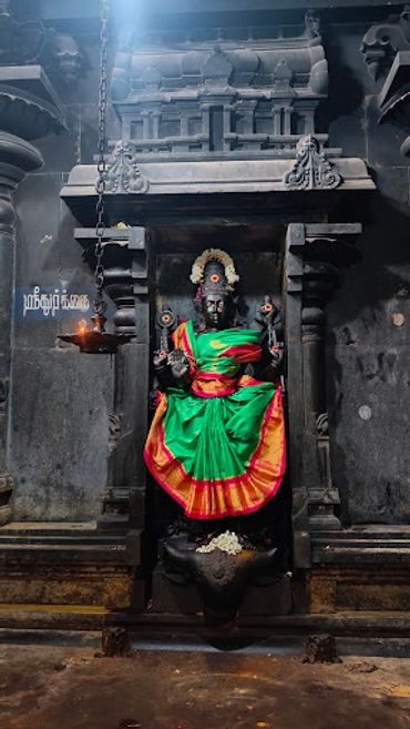 Ancient Hindu deity statue dressed in vibrant cloth inside a temple.