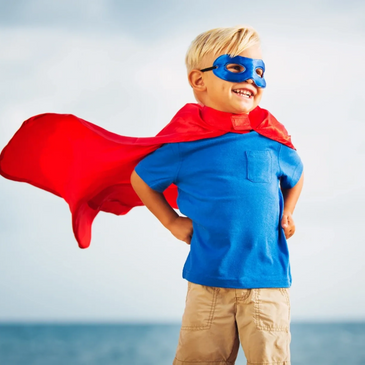 5-year-old Caucasian boy with superhero cape and eye mask standing proudly
