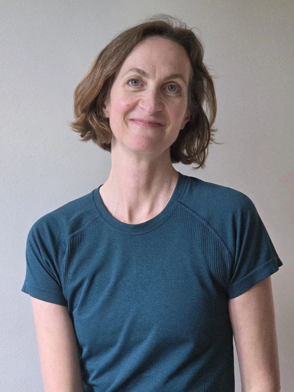 Woman with short brown hair wearing a blue t-shirt smiles gently.