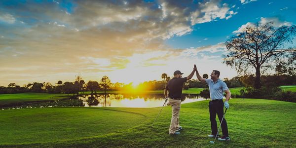 Two men high-fiving on a golf course at sunset.