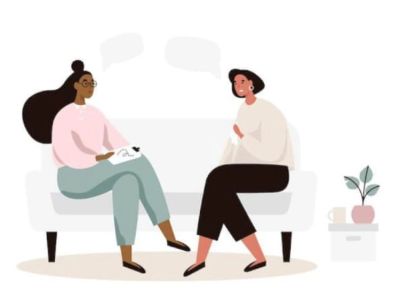 Two women talking on a couch, one taking notes.