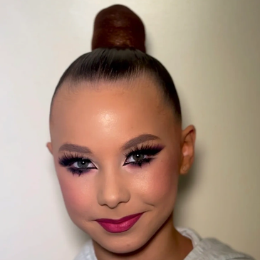 Smiling girl with dramatic makeup and top bun hairstyle.