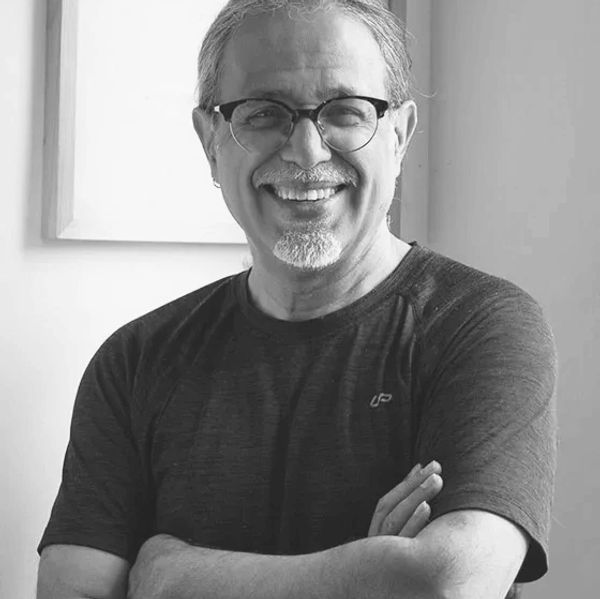 Smiling man with glasses in a dark t-shirt, arms crossed, in black and white.