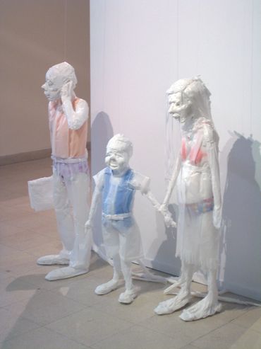 3 life-sized human sculptures made of white trash bags, featuring a child between a woman and a man.