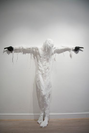Humanoid sculpture made from white trash bags with outstretched arms and pointing black-gloved hands