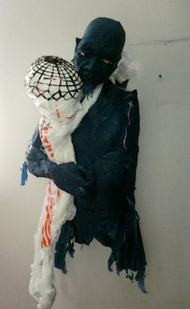Blue plastic bag sculpture of a figure cradling a white child figure with a cap-like patterned head.
