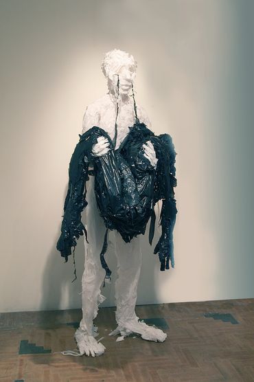 White trash bag sculpture crying black tears that connect its face to a held bundle of black bags.