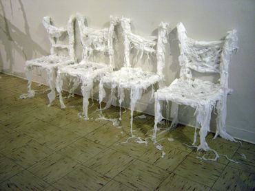 A sculpture of four chairs against a white wall, made of shredded white trash bags.