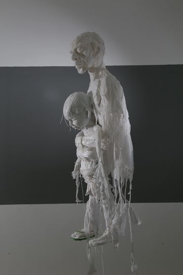 Sculpture by Khalil Chishtee of an adult standing behind a child, made from white trash bags.