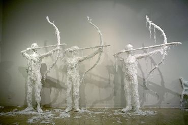 Three life-sized human sculptures made from white trash bags, holding bows and arrows about to shoot
