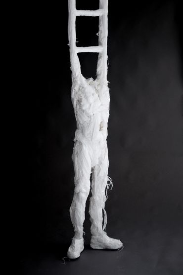 Humanoid sculpture with a ladder replacing its upper body, made from white trashbags.