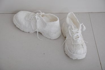Sculpture of two sneakers made of white trash bags, one displayed horizontally and one vertically.