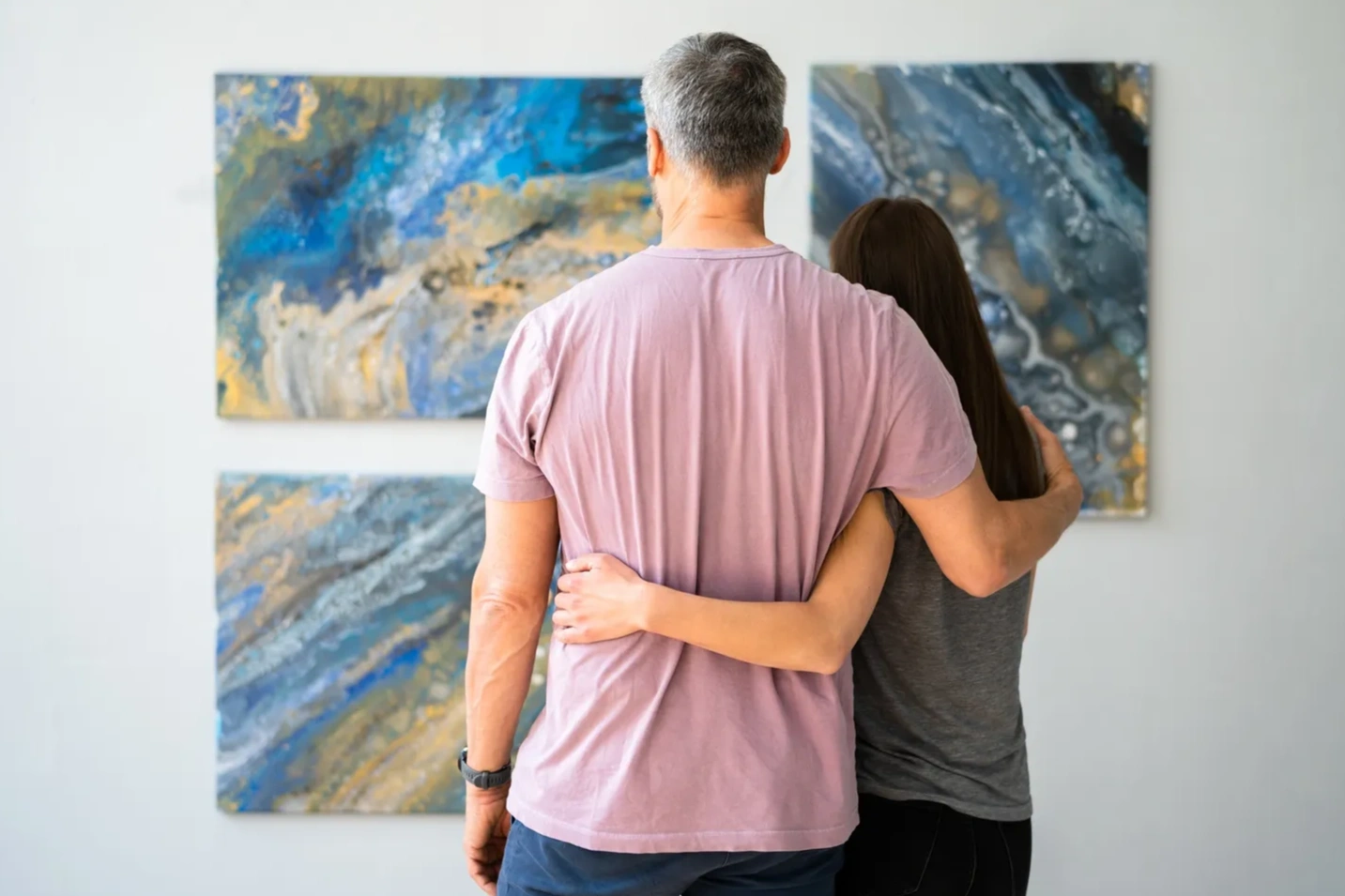 A couple holding each other looking at colourful abstract artwork on a wall