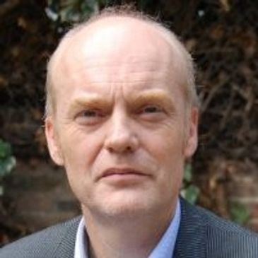 Portrait of a middle-aged man in a formal jacket against a natural background.