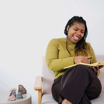 Smiling woman writing in a journal while sitting on a chair in a cozy room.