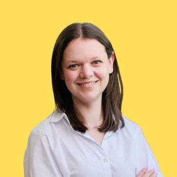 Smiling woman with dark hair in a white shirt against a yellow background.