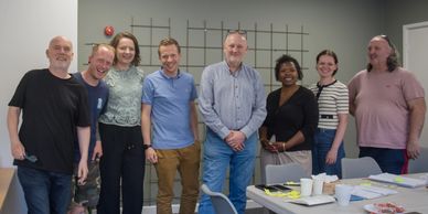 A diverse group of eight people smiling in a casual meeting room.