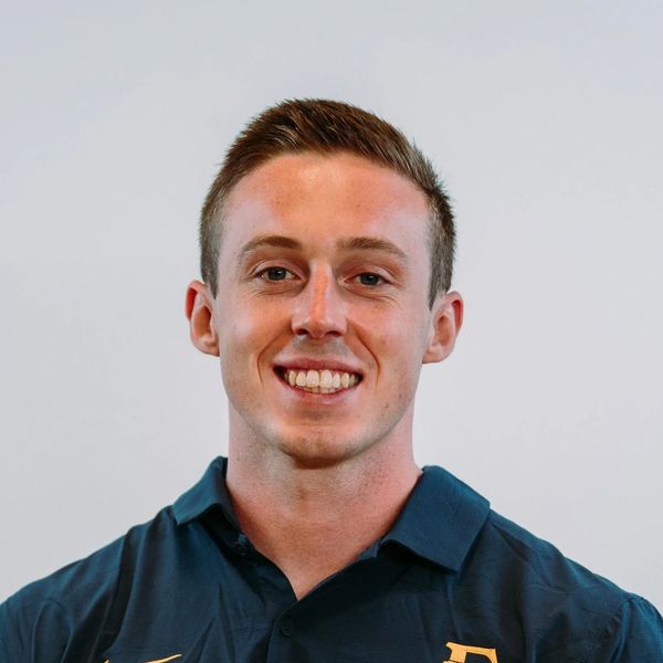 Smiling young man wearing a dark polo shirt with a yellow Nike logo and an 'E' emblem.