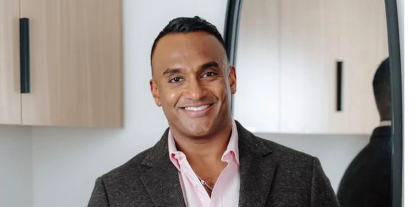 Smiling man in a dark blazer stands confidently in a modern kitchen.
