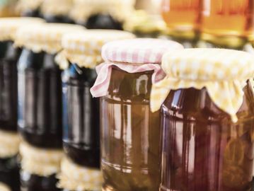 Jars of homemade jam with fabric covers on a shelf.