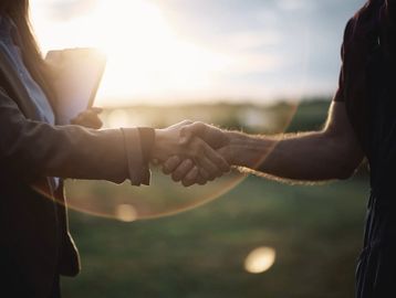 Two people shaking hands outdoors during sunset.