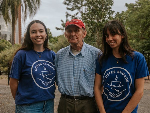 Two young women volunteers smile with an older homeless man