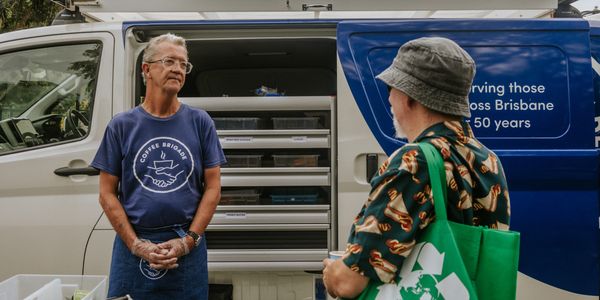 A male volunteer smiles with a homeless man and serves him a sandwich