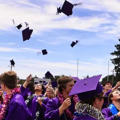 Graduates in purple gowns tossing caps in celebration outdoors.