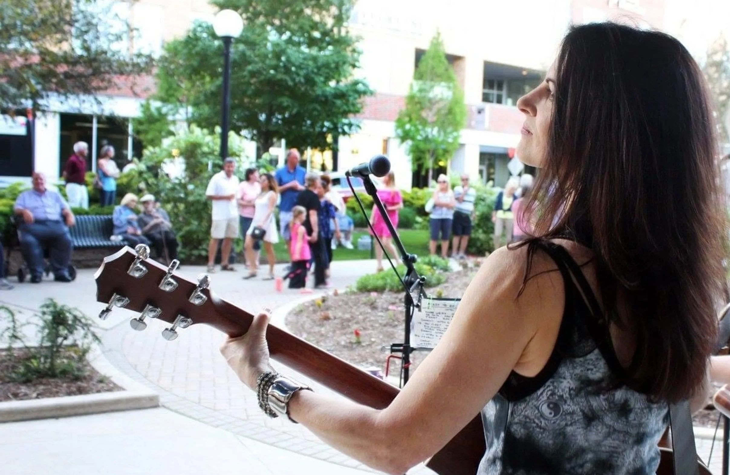 A woman playing guitar at an outdoor event with an audience.