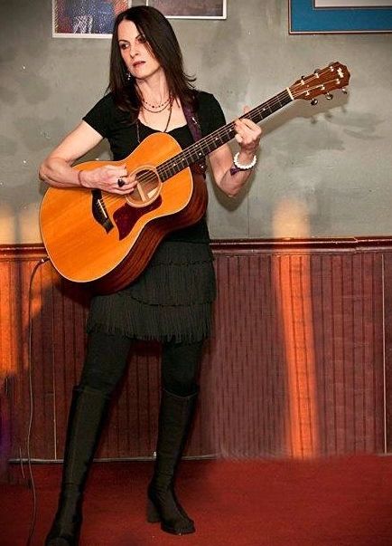 Woman playing an acoustic guitar in a cozy indoor setting.