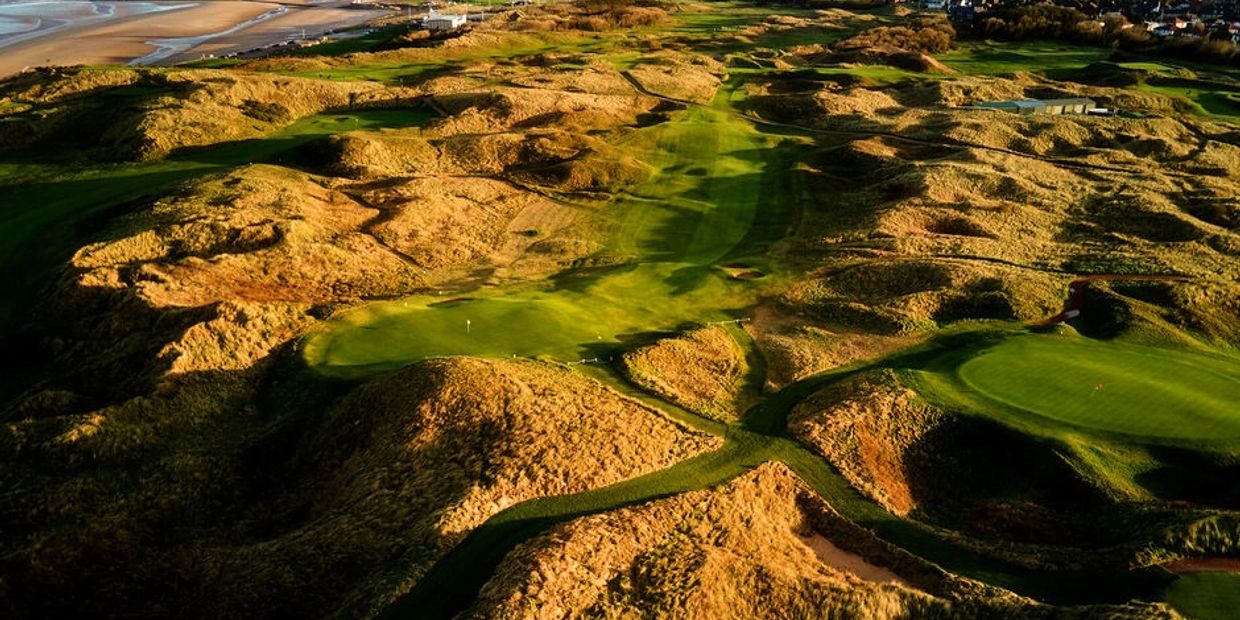 Scenic golf course with hilly terrain near a beach.