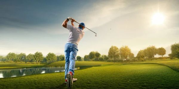 Golfer swinging club on green course at sunset.