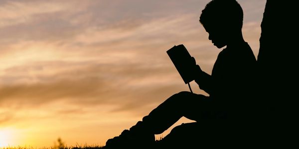 Young boy in silhouette sitting outside reading at sunset