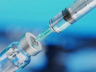 A syringe drawing liquid from a vaccine vial on a blue background.