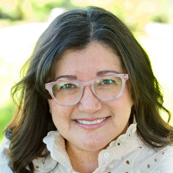 Smiling woman with glasses and dark hair outdoors.