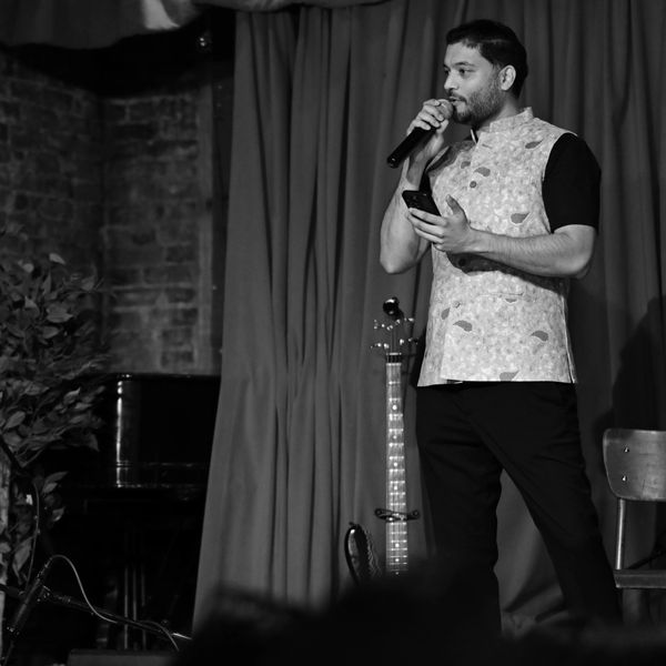 Man speaking into microphone on stage holding a phone.